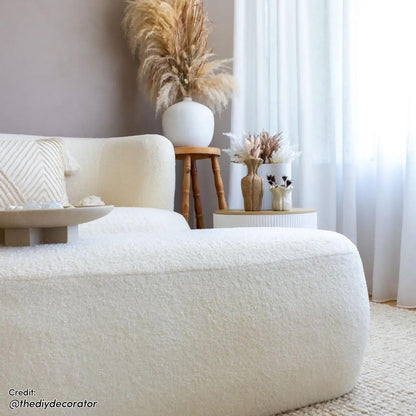 Jamie 110cm Boucle Fabric Ottoman in Cream White, set in a minimalist boho-inspired living space with a textured rug and pampas grass, exudes elegance and cozy relaxation.
