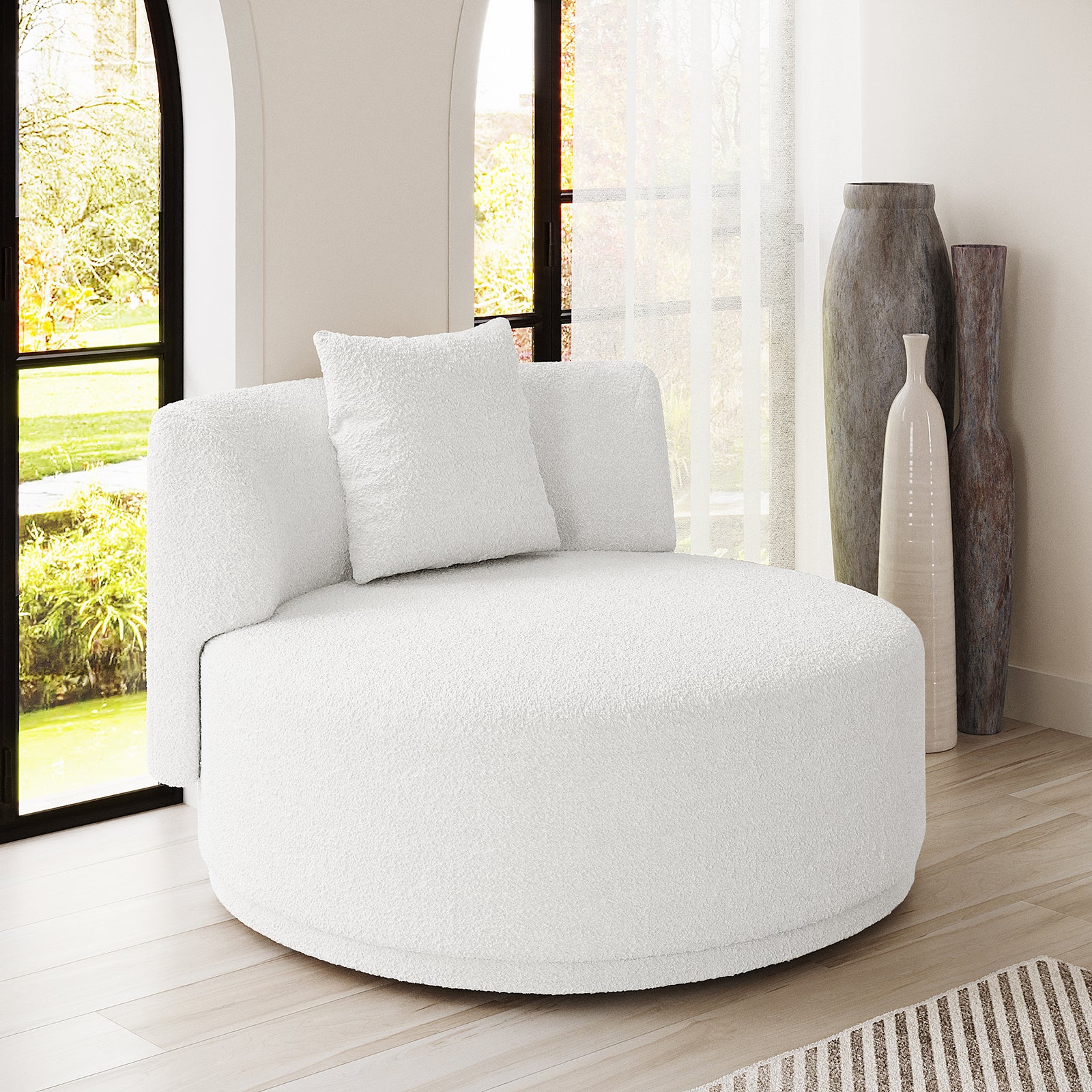 Lyana Single Seater Bouclé Sofa in Cream White, a round, plush lounge chair with matching pillow, set on light wood flooring alongside tall windows and decorative vases, exuding minimalist elegance.