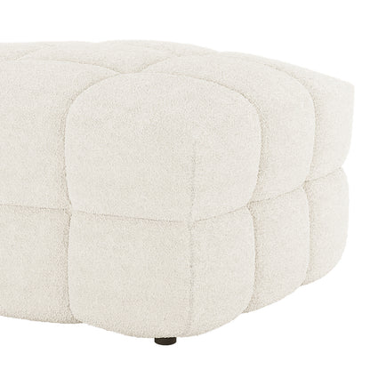 The Norah Boucle Ottoman in Cream White features a low, round design with quilted square panels in bouclé fabric, showcasing a small, dark foot at the base.