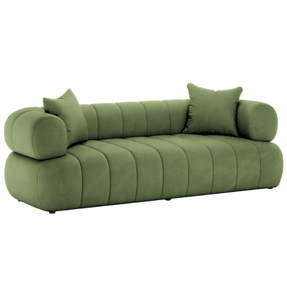 Samira 3 Seater Velvet Sofa in Prasinous Green features a modern, low-profile design with plush channel-stitched upholstery, cylindrical bolster armrests, and matching throw pillows, emphasizing gentle curves and sculptural elegance.