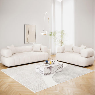 Samira 5 Seater Velvet Sofa Set in Cream, featuring low-profile sofas with cylindrical bolster arms, matching throw pillows, and plush cream velvet upholstery, elegantly arranged in a bright, minimalist living room.