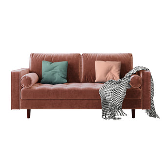 Sollia 3-Seater Velvet Sofa in Blush on a brown couch, adorned with a green pillow and a black and white blanket, highlighting its luxurious velvet texture and elegant design.