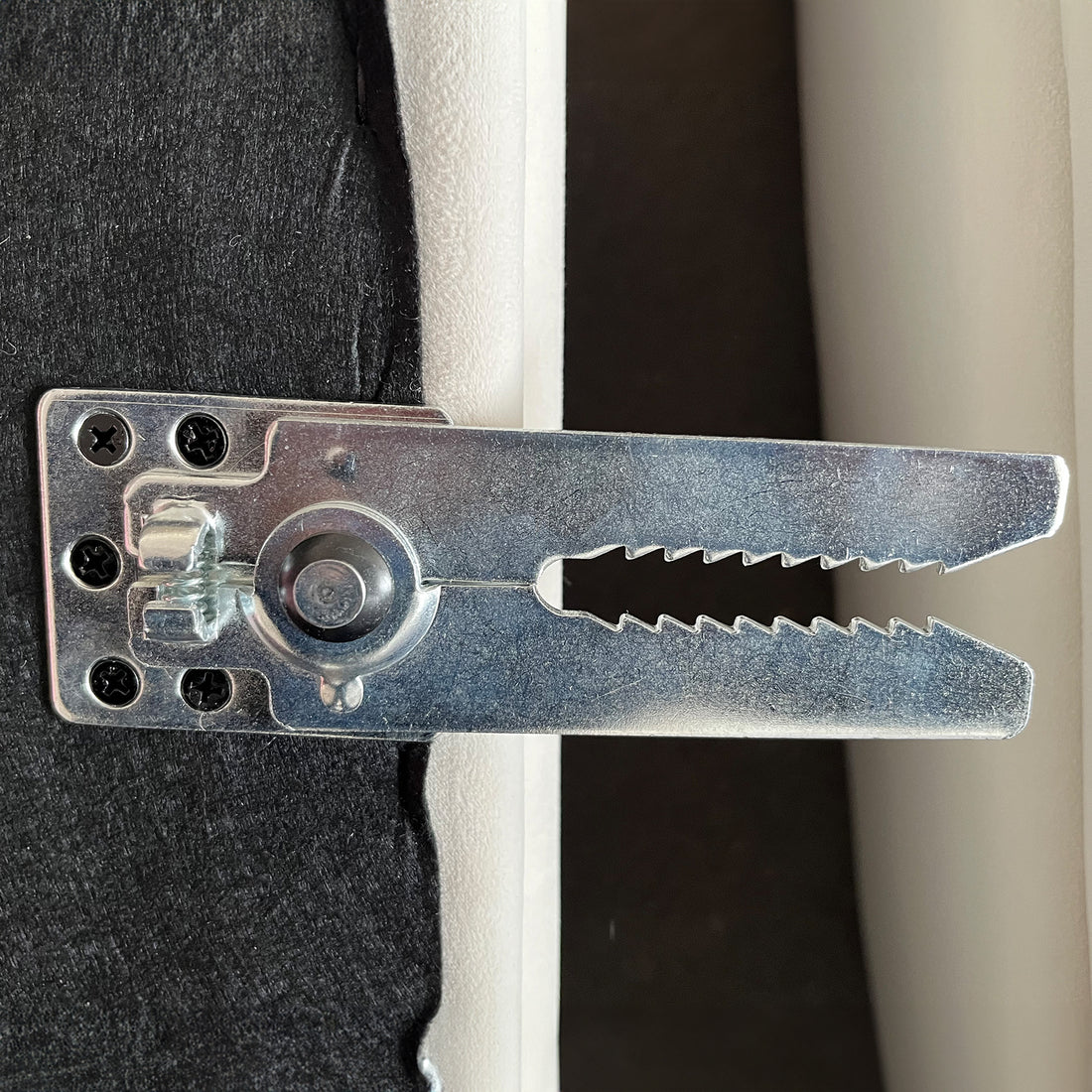 Close-up of metallic crocodile clip hardware with serrated jaws and mounting plate with screws, attached to black fabric edge