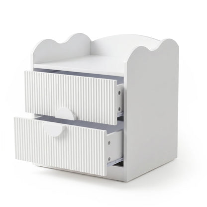 A white bedside table with a scalloped-edge top and two drawers featuring fluted fronts and semi-circular handles.