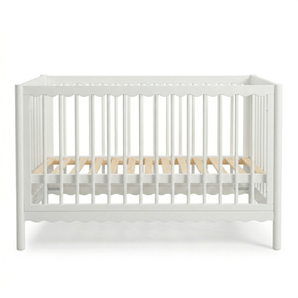White wooden baby crib with scalloped edges and natural wood mattress slats on a white background