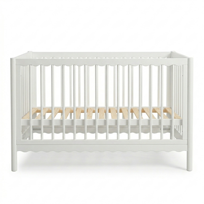 White wooden baby crib with scalloped edges and natural wood mattress slats on a white background