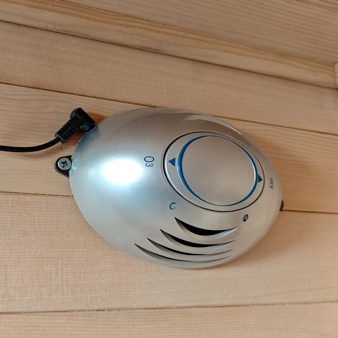Oval electronic device mounted on a wooden wall with visible cord