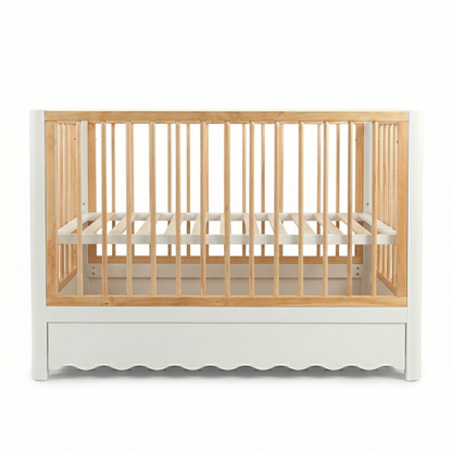 Front view wooden baby crib with scalloped white base and natural wood slats on white background
