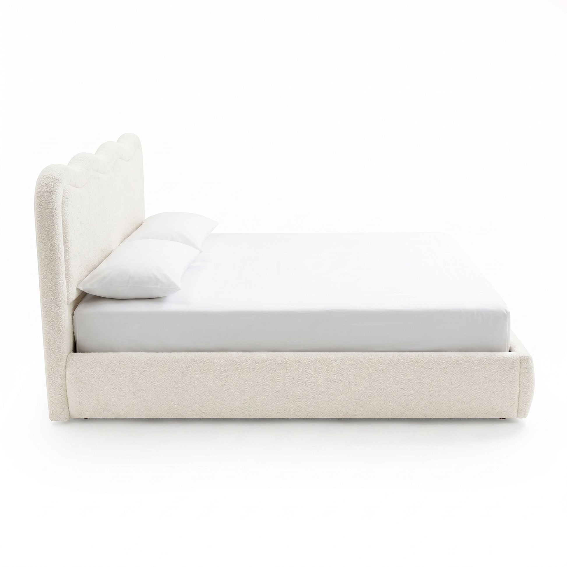 Side profile of an upholstered bed with scalloped headboard on white background
