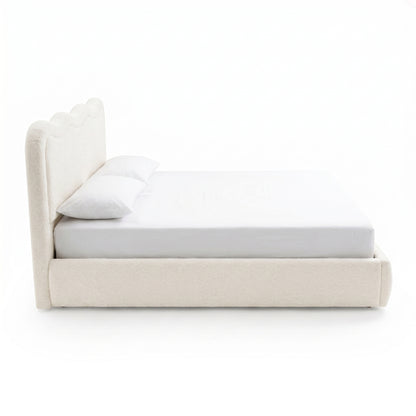 Side profile of an upholstered bed with scalloped headboard on white background