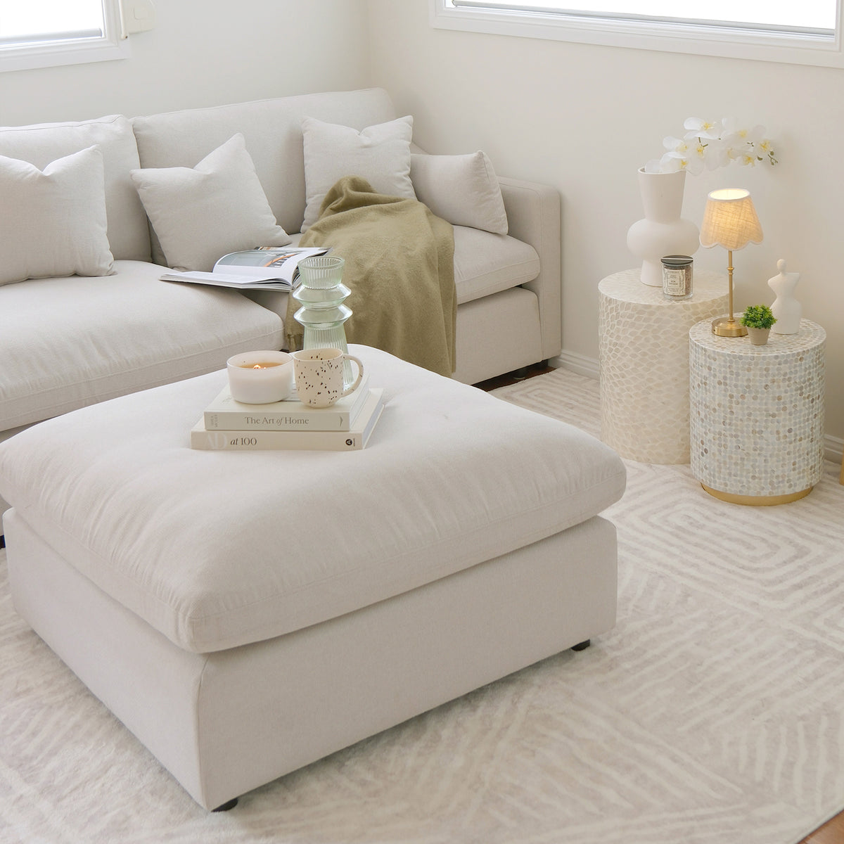 Light-colored sectional sofa with matching ottoman in a bright modern living room.