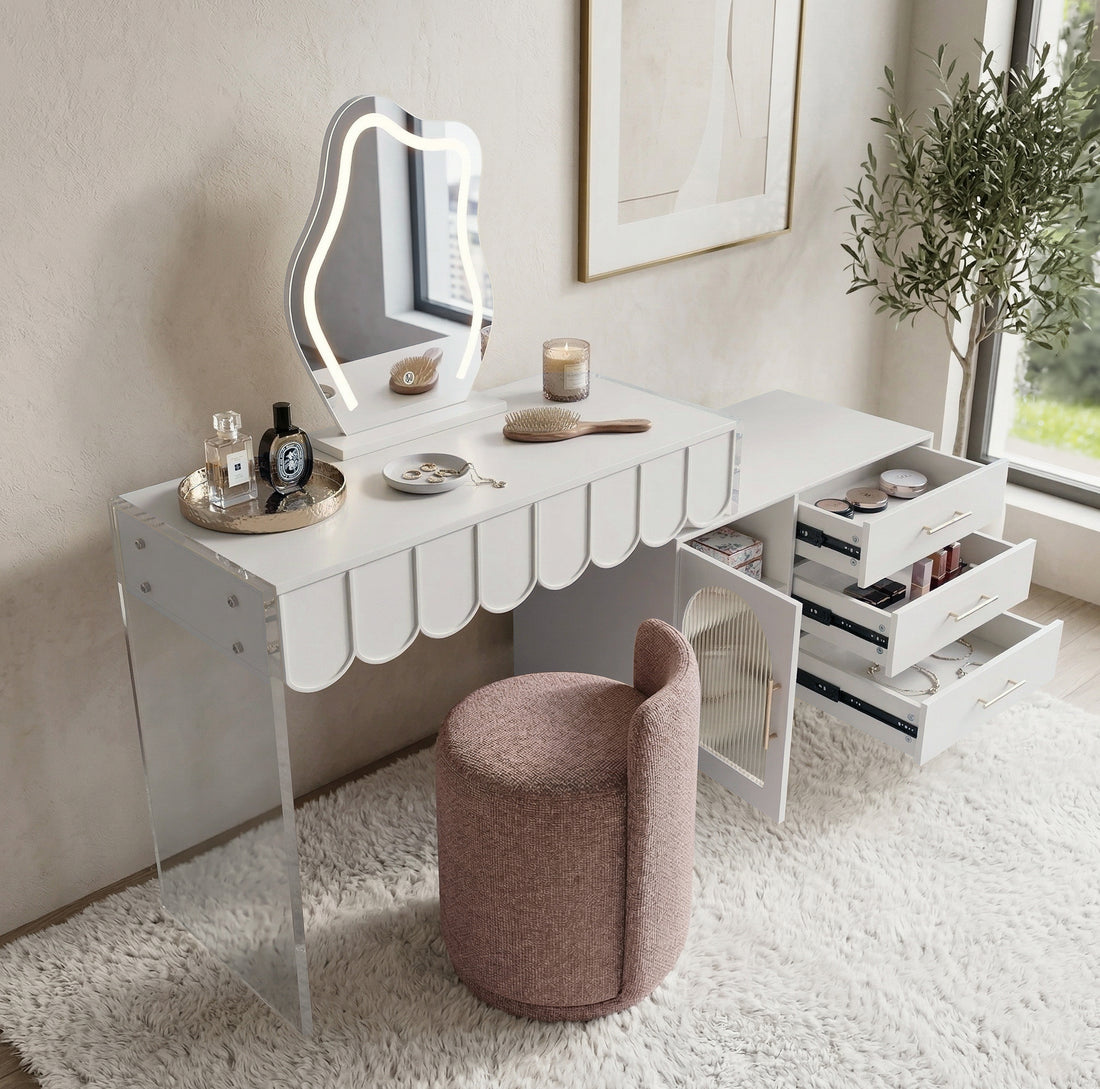 Lifestyle shot of the white scalloped-edge vanity with backlit mirror and pink stool on a textured rug near window and plant