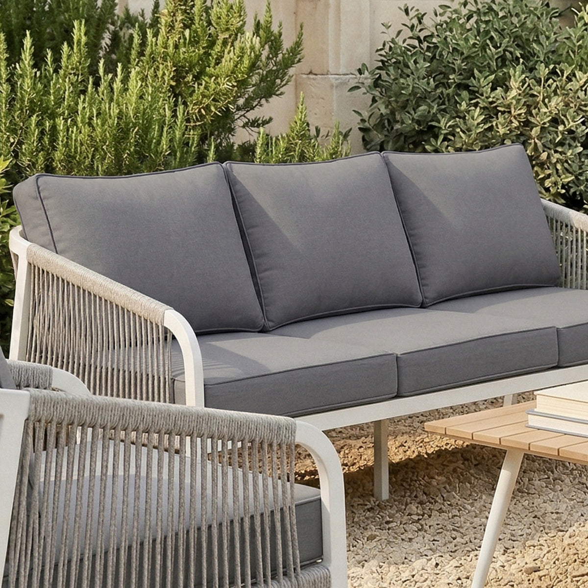 Vernon Outdoor Cushion Covers Set of 5 in Grey adorn a modern loveseat with slate-gray cushions, harmonizing with a white metal frame and woven rope design on a gravel patio.