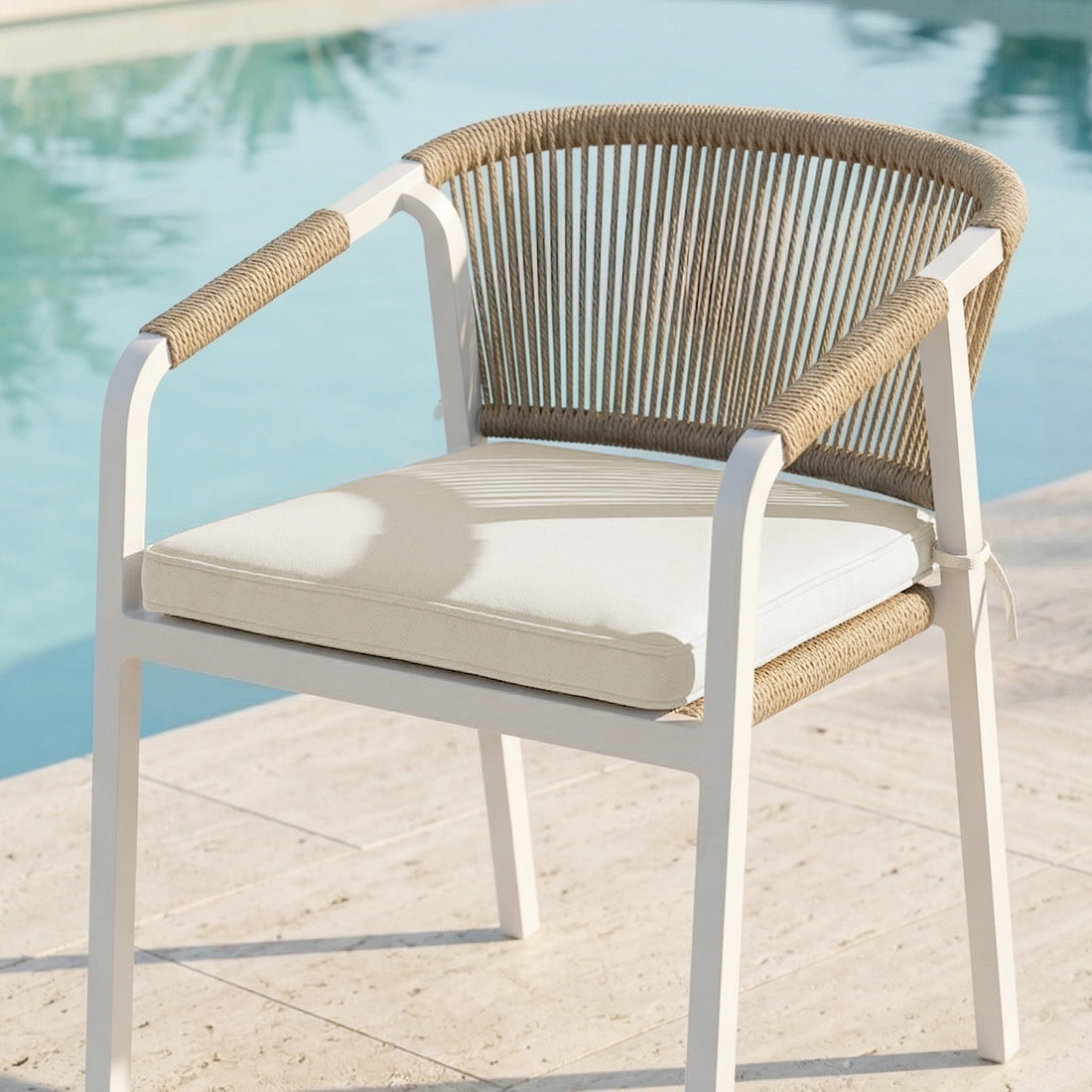 Vernon Outdoor Dining Chair Covers in Cream White on a modern outdoor armchair by a pool, featuring a white metal frame and rope-woven design, enhancing and protecting your outdoor setting.