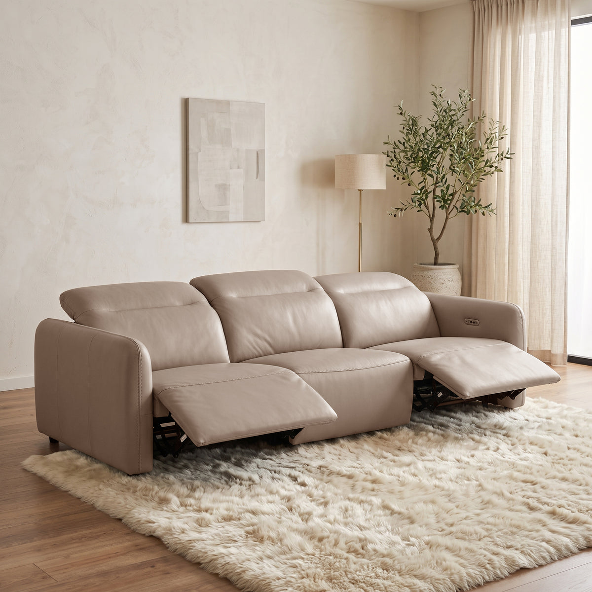 Beige sectional reclining sofa in a living room with rug, lamp, plant, and natural light