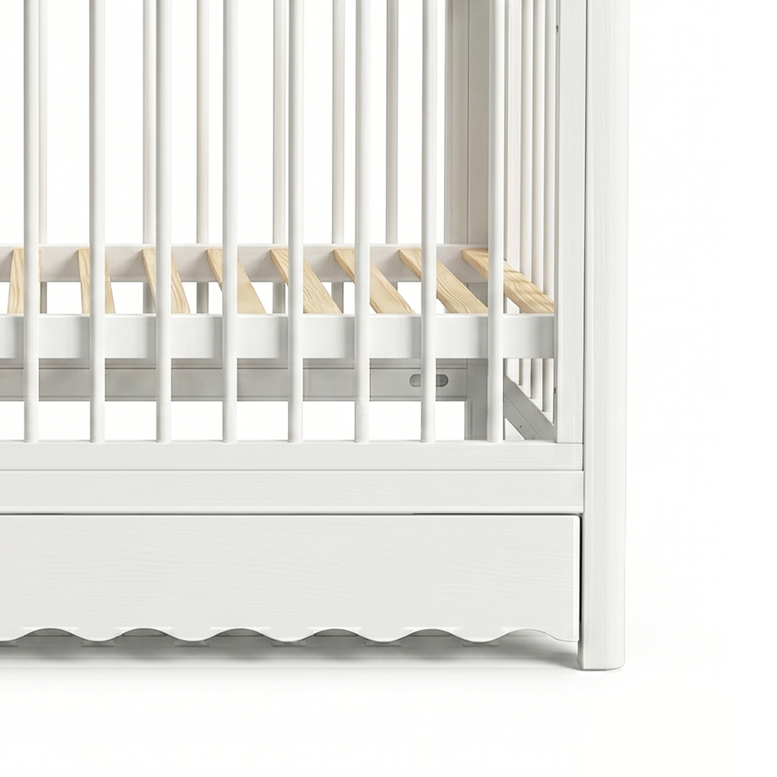 Partial view of lower section of white baby crib with scalloped base and visible mattress supports