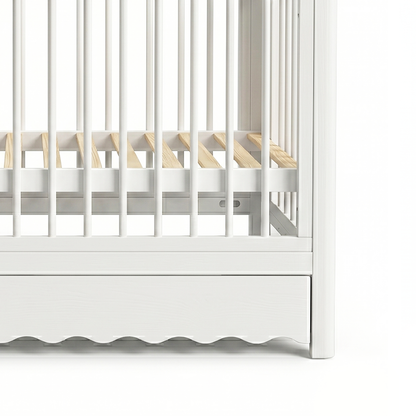 Partial view of lower section of white baby crib with scalloped base and visible mattress supports