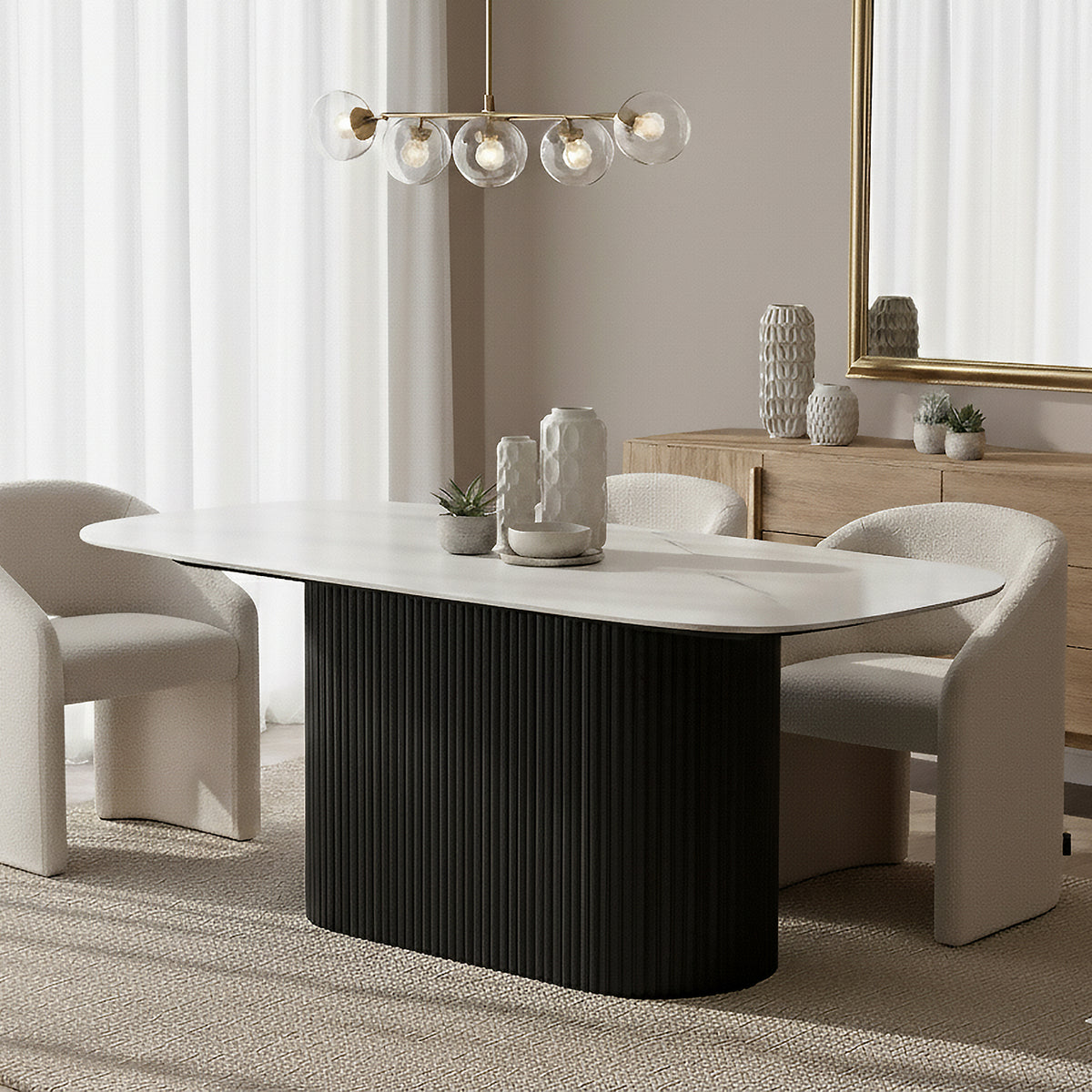 Aeris 180cm Marble Look Dining Table With Wood Base in Black, featuring an elegant white oval tabletop on a fluted black pedestal, surrounded by off-white boucle chairs and accented with sculptural vases.