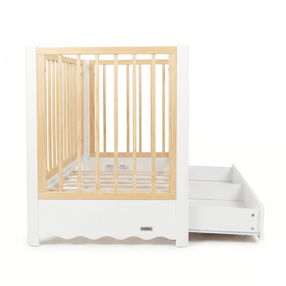 Modern white and natural wood baby crib with attached drawer unit on white background