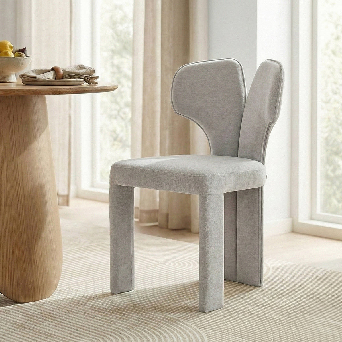 Two light gray upholstered chairs by a wooden dining table in bright room
