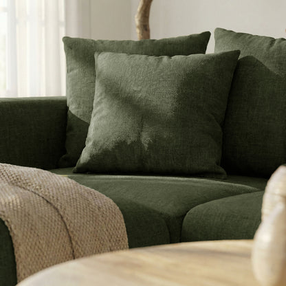 Close-up corner of dark green sectional sofa with pillows and throw in a bright room