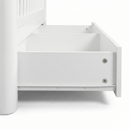 Close-up of bottom corner of white crib with open storage drawer on white background