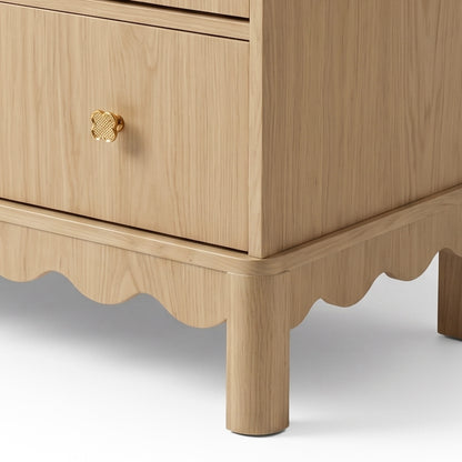 Lower corner of wooden furniture piece showing scalloped base and gold handle on white background