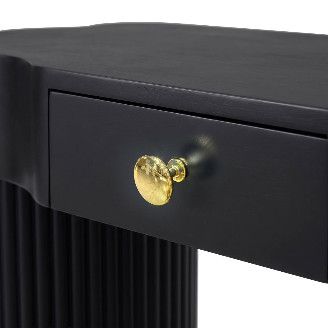 Close-up of black furniture drawer with gold knob and fluted side detail on a white background